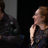 Judith Keller sits at the microphone and smiles, next to her sits Johannes Becker
