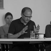 Black and white photograph of Bojan Jović. He is sitting at a conference table and gesticulates.