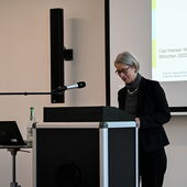 Hania Siebenpfeiffer steht am Rednerpult vor einer Leinwand und trägt vor.