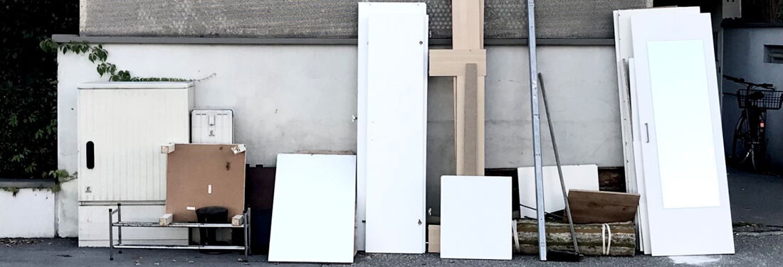 Verschiedene Möbelteile stehen an eine Wand gelehnt auf einem Bürgersteig an einer Straße mit Gulli.