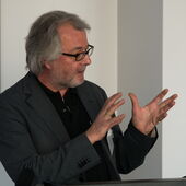 Martin Treml trägt hinter dem Vortragspult vor und gestikuliert