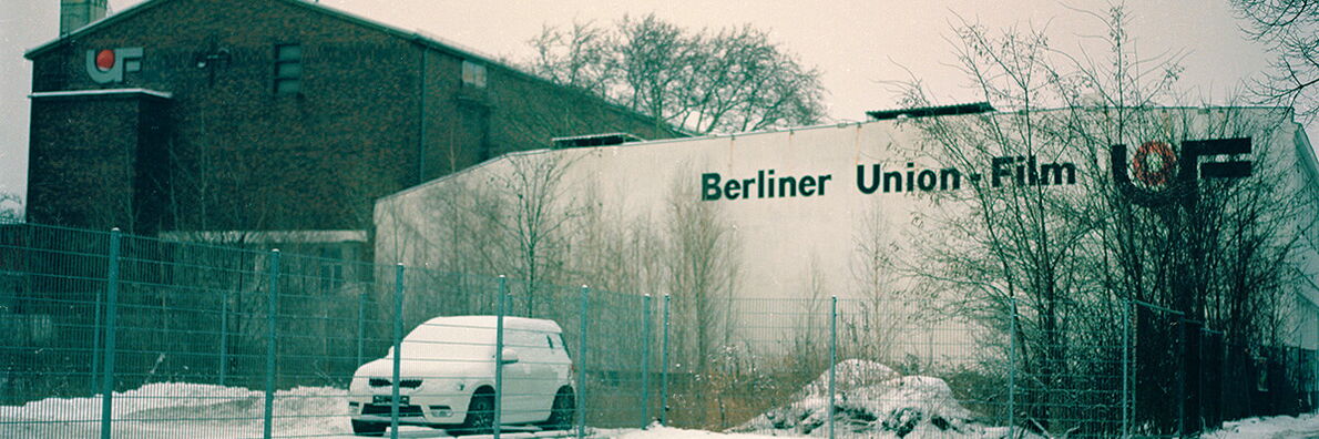 Gebäude der Berliner Union Film im Winter mit einem verschneiten Auto und kahlen Bäumen im Vordergrund.