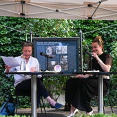 Eva Geulen and Teresa Präauer are sitting on a stage. Eva Geulen looks at her documents, Teresa Präauer laughs.