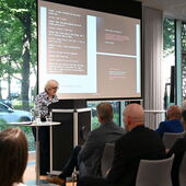 Anne-Kathrin Reulecke steht am Rednerpult, hinter ihr ihre PowerPoint-Präsentation mit heller Schrift auf schwarzem Grund.