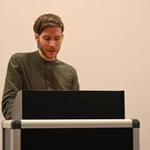 A person in a green shirt—award winner Georg Simmerl—stands at the speaker’s desk.