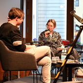 Elias Hirschl and Hanna Hamel sit on a podium. Hanna Hamel speaks into a microphone while looking at Elias Hirschl.