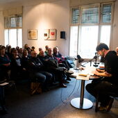 Saša Stanišić reads on a stage in front of a very well attended audience, Stefan Willer sits next to him