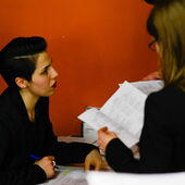 Two participants of the event: one writes something down, the second reads in the event brochure