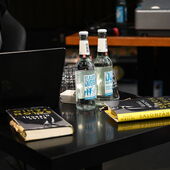 Two Salonfähig-issues and two water bottles in front of a laptop on a black table.