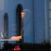 Durch ein Fenster ist Alexandra Cárdenas an ihrem Laptop stehend zu sehen.