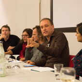 Torsten Michaelsen sits at a conference table and gestures during a speech. Other conference participants listen to him.