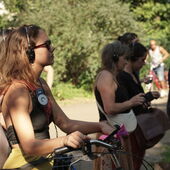 Several people stand along a path in Volkspark Hasenheide and are listening to Cord Riechelmann’s guided tour using a headset. The person in the front leans on their bicycle.