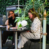 Emma Braslavsky and Hanna Hamel are sitting on a stage with a flowering plant in the foreground.
