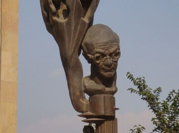 Bronzestatue des Philosophen Merab Mamardashvili vor blauem Himmel. Rechts ragen Zweige ins Bild.