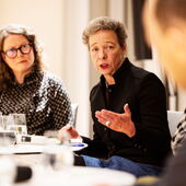 Katja Weber und Eva Geulen sitzen an einem Bistrotisch und schauen nach links in die Runde, Eva Geulen spricht und gestikuliert.