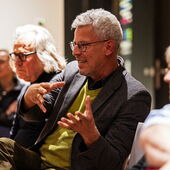 Ein Zuhörer aus dem Publikum stellt gestikulierend eine Frage an das Podium.