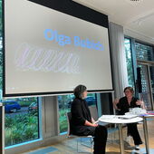 Olga Bubich und Tina Wünschmann sitzen vor der Leinwand, auf der Bubich's Name steht.