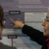 Stefanie Jannedy steht neben einem Teilnehmer, zeigt auf ein Poster und erklärt