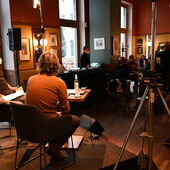 The authors Philipp Schönthaler and Hannes Bajohr and the moderator Morten Paul are sitting on a podium and can be seen from behind. The audience is seated in the background.