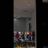 Blick von der Straße in den Veranstaltungsraum, es sind voll besetzte Publikumsreihen zu sehen.