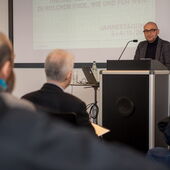 Claude Haas hält eine Rede vor Publikum, hinter ihm läuft eine Präsentation