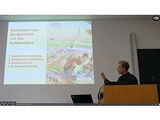 Matthias Schwartz stands at the lectern and points to his presentation.