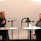 Matthias Schwartz und Olga Grjasnowa sitzen einander gegenüber an kleinen weißen runden Tischen auf roten Stühlen. Schwartz spricht in ein Mikrofon, Grjasnowa hört im zu.