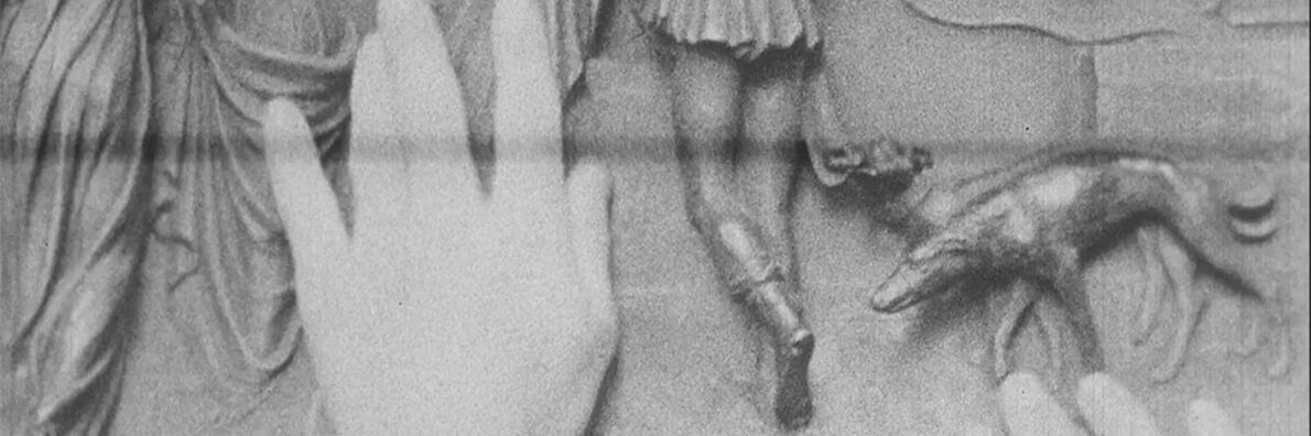 Two hands touch a relief on which several human lower bodies can be seen from behind and a dog on a leash.