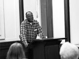 Black and white photograph of Babafemi Adeyemi Osofisan during a lecture. He stands at the lectern and speaks to the crowd.
