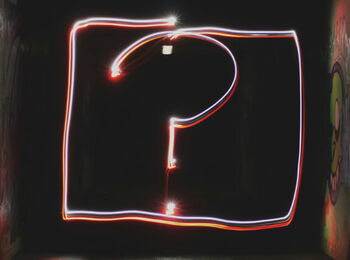 Leuchtendes Fragezeichen aus roten und weißen Lichtspuren in einem dunklen, mit Graffiti besprühten Tunnel.