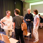 Katrin Trüstedt is talking between the rows of chairs in the seminar room with a person who can be seen from behind. Matthias Schwartz and Eva Axer are standing to the right and are talking.