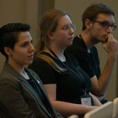 Drei Teilnehmer*innen sitzen und hören einem Vortrag zu