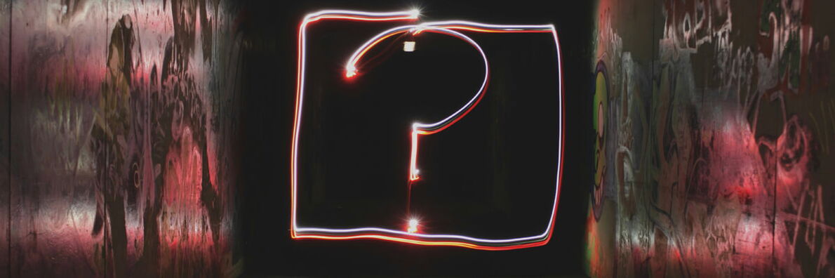 Glowing question mark made of red and white light trails inside a dark, graffiti-covered tunnel.