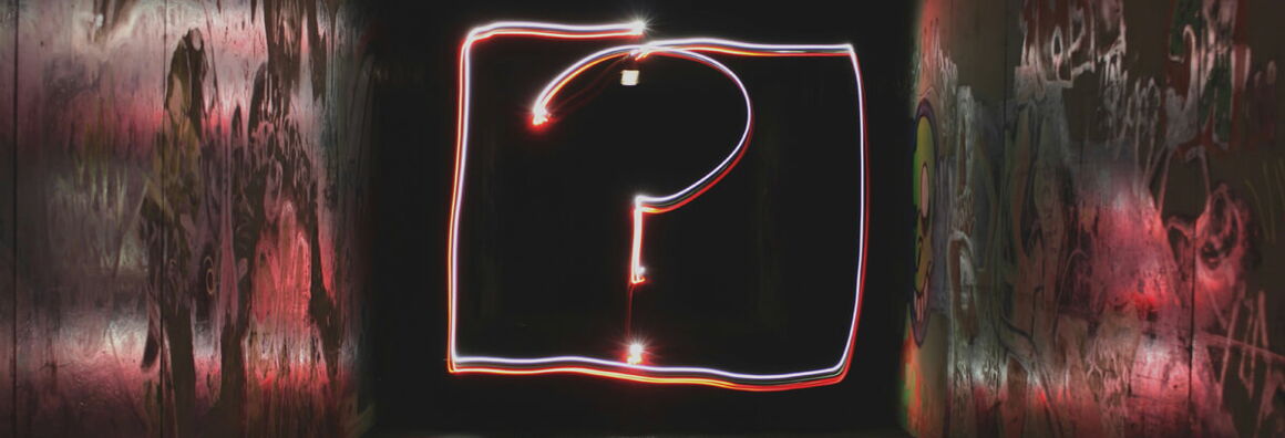 Leuchtendes Fragezeichen aus roten und weißen Lichtspuren in einem dunklen, mit Graffiti besprühten Tunnel.