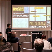 Magdalena Gronau steht vor einer Leinwand und spricht zum Publikum. In ihrer Präsentation sind u.a. Aufnahmen verschiedener Archivobjekte zu sehen.