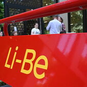 Detailansicht eines roten Plakataufstellers mit dem Schriftzug »Li-Be«, im Hintergrund unscharfe Personen.