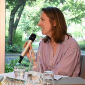 Kira Jürjens spricht in ein Mikrofon und ist nach links gewendet.