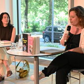 Lin Hierse und Sonja Longolius sitzen nebeneinander an weißen Bistrotischen und unterhalten sich. Vor Longolius stehen Hierses Bücher auf dem Tisch.