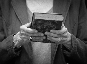 Zwei ältere Hände mit Ringen an den Fingern halten ein Buch.