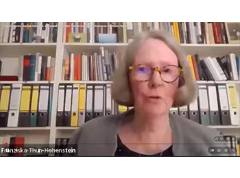 YouTube-Screenshot von Franziska Thun-Hohenstein mit Hornbrille vor einem Regal mit Aktenordnern und Büchern.