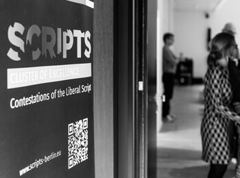 Entrance to the Eberhard Lämmert Hall. On the left is a poster of the “SCRIPTS” cluster of excellence, on the right blurred figures.